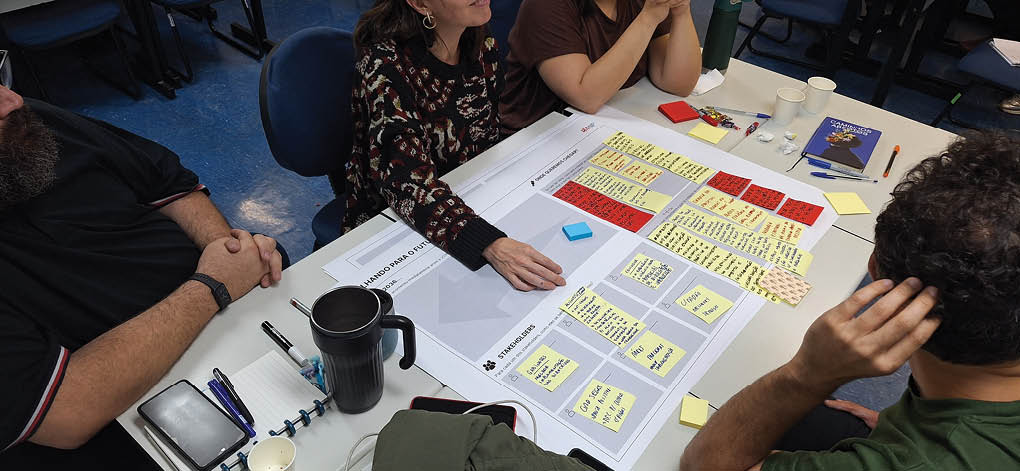 A group of people are sitting around a table with a white board. Description generated by AI