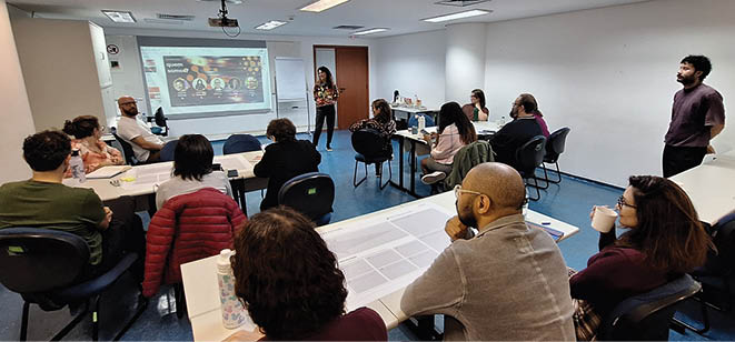 A group of people are sitting in a room, looking at a projector screen. Description generated by AI